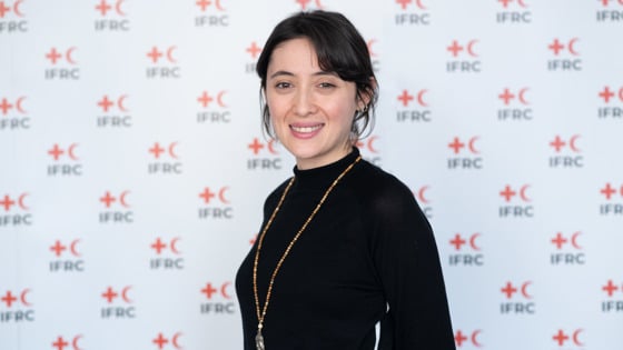 Fatma Nur smiles and looks at the camera. She's standing in front of an IFRC photo background.