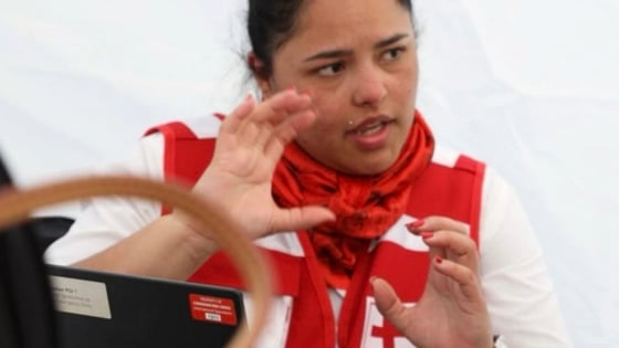 Lina Garcia is talking and moving her hands, while wearing a Red Cross jacket and looking away from the camera.