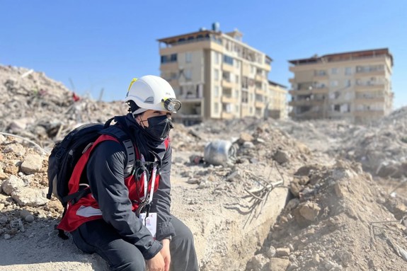 Sharifah Yousef Al-Bounagh with a helmet and a Red Crescent Vest in building rubble