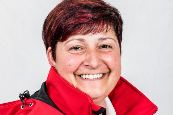 Sylvia is looking into the camera and is smiling. She has short hair and is wearing a red jacket.