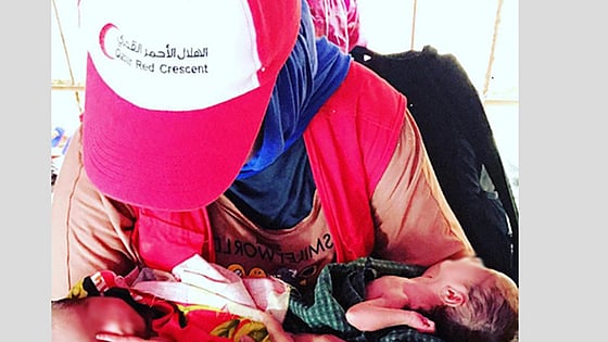A woman with a Red Crescent cap is holding babies