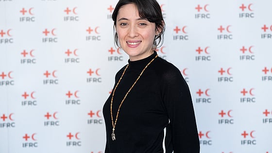 Fatma Nur smiles and looks at the camera. She's standing in front of an IFRC photo background.