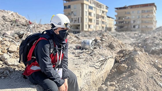 Sharifah Yousef Al-Bounagh with a helmet and a Red Crescent Vest in building rubble