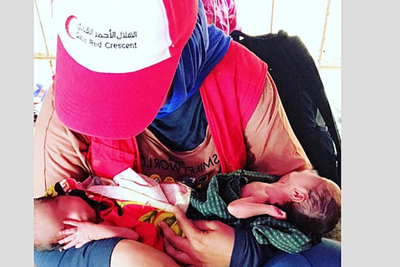 A woman with a Red Crescent cap is holding babies