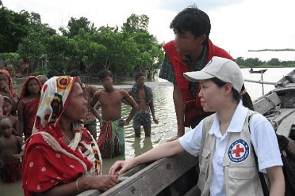 Side profile of a woman wearing a cap and a red cross west