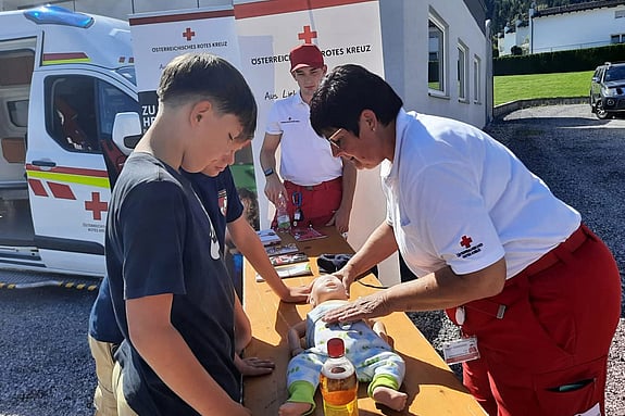 Sylvia is showing a young boy how to deliver first aid to a doll that is meant to represent a newborn.