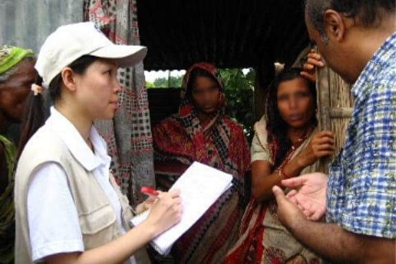Woman writing in a block while two women are standing in the background