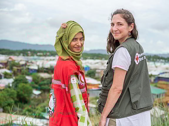 Two upturned women smiling at the camera with a landscape in the background