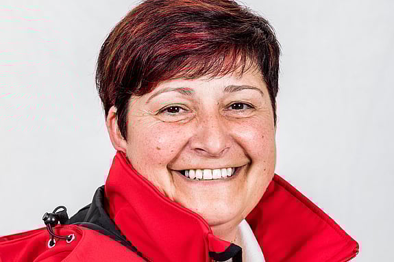 Sylvia is looking into the camera and is smiling. She has short hair and is wearing a red jacket.