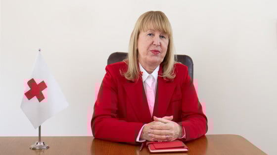 Tanya Petrova Georgieva is sitting at a desk next to a small Red Cross flag and wearing a red vest.